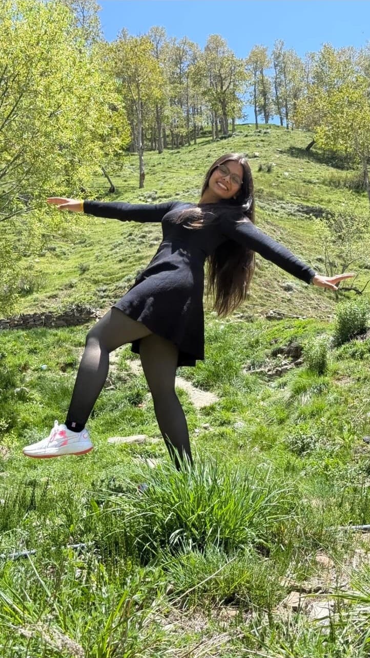 Riya with her arms out in a mountain meadow
